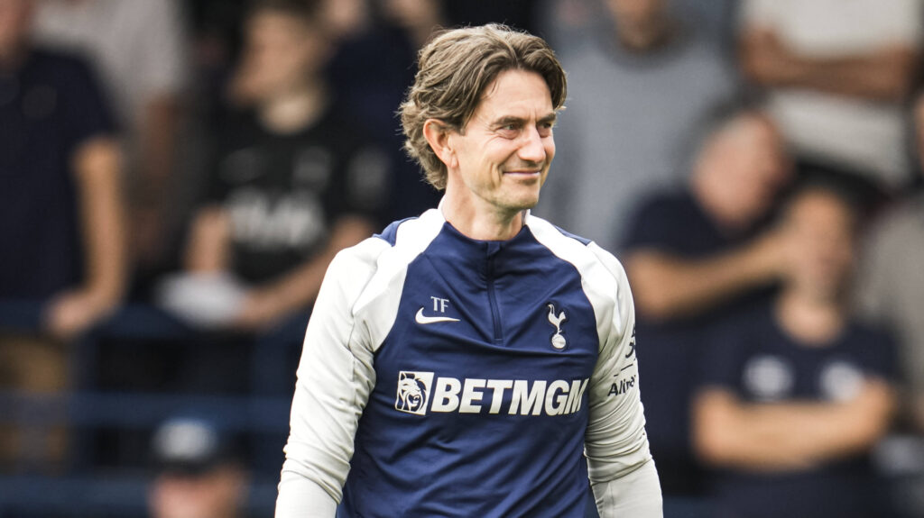 Tottenham manager Thomas Frank smiles while glancing to his right.